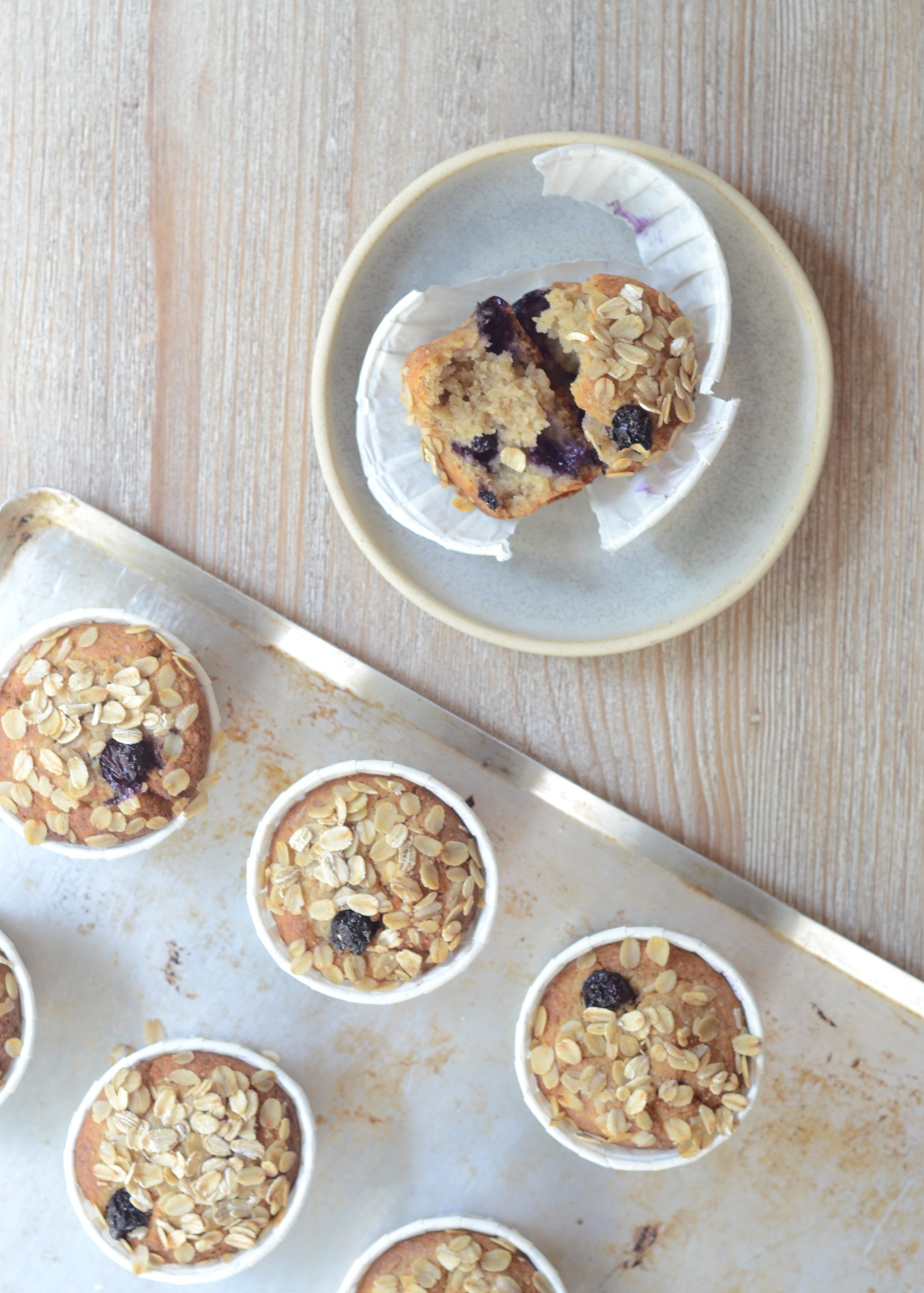 Bandeja con muffins de platano canario y avena sobre una bandeja de pastelería y un muffin cortado al medio donde se ve la textura migosa